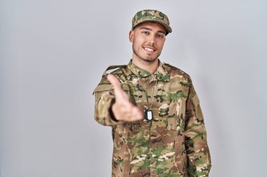 Kamuflaj üniforması giyen genç İspanyol adam dostça gülümseyerek selamlaşma ve hoş geldin diyor. başarılı iş. 