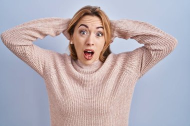 Mavi arka planda dikilen İspanyol kadın deli ve elleri başının üstünde korkmuş, korkmuş ve ağzı açık şoktan şaşırmış. 