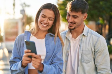 Genç adam ve kadın çift sokakta akıllı telefon kullanarak gülümsüyor.