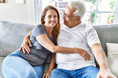 Orta yaşlı İspanyol çift mutlu bir şekilde gülümsüyor ve evdeki kanepede oturup sarılıyorlar..