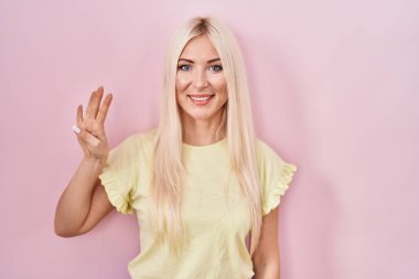 Caucasian woman standing over pink background showing and pointing up with fingers number four while smiling confident and happy. 