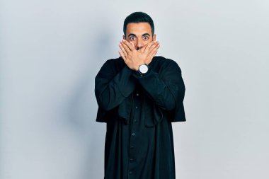 Katolik rahip cübbesi giyen yakışıklı, sakallı, ağzı yanlışlıkla ellerle kapatan bir İspanyol. gizli kavram. 