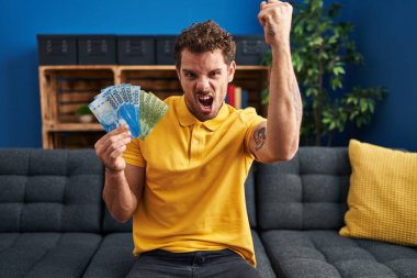 Şili pesolarını tutan genç İspanyol adam öfkeyle bağırıyor, öfkeyle bağırıyor ve el kaldırıyor. 