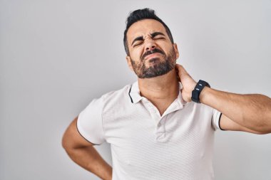 Young hispanic man with beard wearing casual clothes over white background suffering of neck ache injury, touching neck with hand, muscular pain 