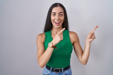 İzole edilmiş arka planda duran genç bir kadın gülümsüyor ve kameraya bakıyor iki eliyle ve parmaklarıyla kenarı işaret ediyor.. 