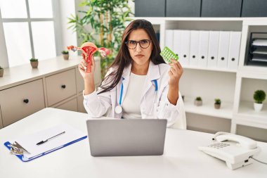 Genç İspanyol doktor kadın anatomik kadın organı ve doğum kontrol hapları tutuyor şüpheci ve gergin, sorun yüzünden surat asıyor. negatif kişi. 