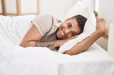 Afro-Amerikalı adam yatakta kendinden emin bir şekilde gülümsüyor.