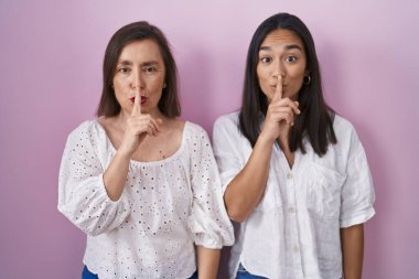 Hispanic mother and daughter together asking to be quiet with finger on lips. silence and secret concept. 