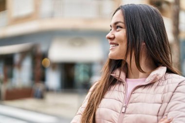 Kendine güvenen genç bir kadın caddede kollarını kavuşturmuş duruyor.
