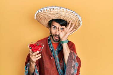 Meksika şapkası takan, kırmızı biber tutan genç İspanyol adam gülümsüyor. 