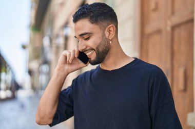 Genç Arap adam gülümsüyor, kendinden emin bir şekilde caddedeki akıllı telefondan konuşuyor.