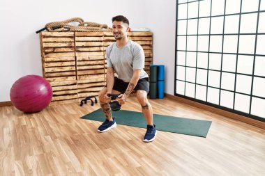 Genç İspanyol adam gülümsüyor spor merkezinde kettlebell kullanıyor.