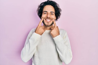 Yakışıklı, beyaz süveter giyen, ağzı açık gülümseyen, parmakları işaret eden ve neşeli gülümsemeye zorlayan İspanyol bir adam. 