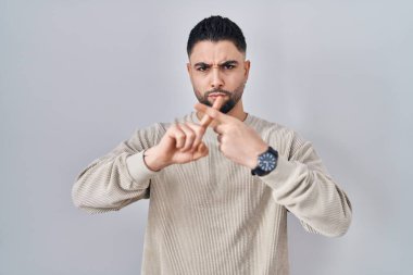 Genç yakışıklı adam izole edilmiş arka planda duruyor. Reddedilme ifadesi negatif işaret vermesi için parmaklarını çapraz yapıyor. 