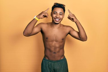 Mayo ve yüzücü gözlüğü takan genç Afro-Amerikalı adam iki eliyle başını gösteren gülümseme, harika bir fikir ya da düşünce, iyi bir hafıza 