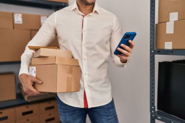 Genç İspanyol bir e-ticaret işçisi ofisteki akıllı telefon paketlerini kullanıyor.