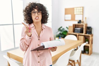 Young middle eastern woman wearing business style at office pointing aside worried and nervous with forefinger, concerned and surprised expression 