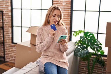 Yeni evde akıllı telefon ve kredi kartı kullanan genç bir kadın.