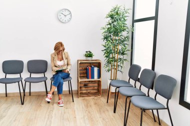 Orta yaşlı sarışın kadın bekleme odasındaki panoya kendinden emin bir yazı yazarak gülümsüyor.