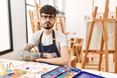 Hispanic man with beard at art studio skeptic and nervous, disapproving expression on face with crossed arms. negative person. 