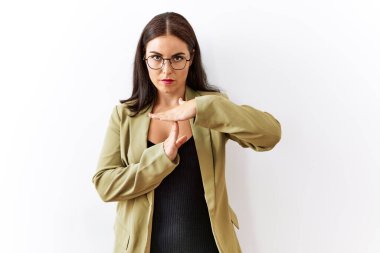 Young brunette woman standing over isolated background doing time out gesture with hands, frustrated and serious face 