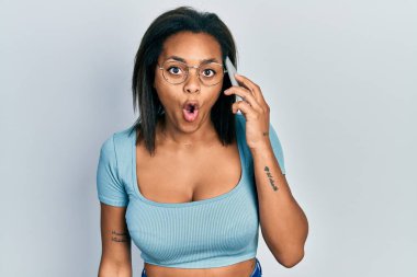 Genç Afro-Amerikalı kız akıllı telefondan konuşuyor. Korkmuş ve ağzı açık bir şekilde şaşırmış, inançsız bir yüz ifadesi. 