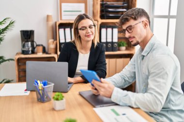 Young man and woman business workers using laptop and touchpad working at office