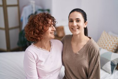 Two women mother and daughter hugging each other sitting on bed 
