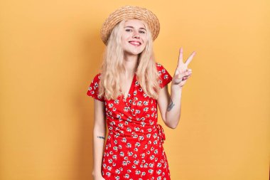 Sarışın, güzel, beyaz bir kadın. Yaz şapkası takıyor. İki numaralı parmaklarıyla işaret ediyor.. 