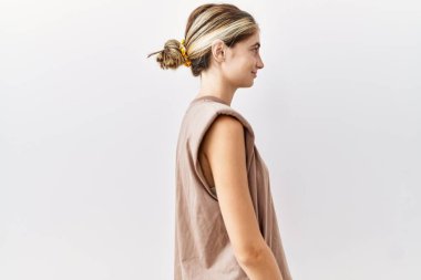 İzole edilmiş arka planda duran genç sarışın kadın yan tarafa bakıyor, rahat poz veriyor kendine güvenen bir gülümsemeyle doğal bir yüz ifadesi sergiliyor.. 