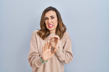 Young woman standing over isolated background disgusted expression, displeased and fearful doing disgust face because aversion reaction. 