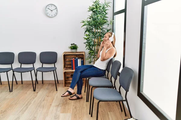 Young caucasian woman listening to music sitting on chair at waiting room