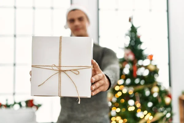 Young Hispanic Man Holding Gift Standing Christmas Tree Home — Fotografia de Stock