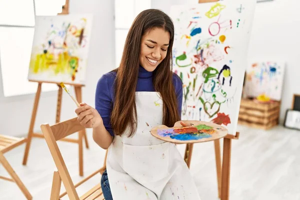 年轻的拉丁女子微笑着 自信地在艺术工作室拿着画笔和调色板 — 图库照片