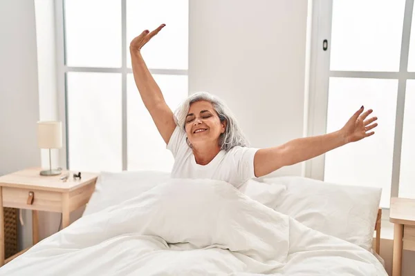 Middle age woman waking up stretching arms at bedroom