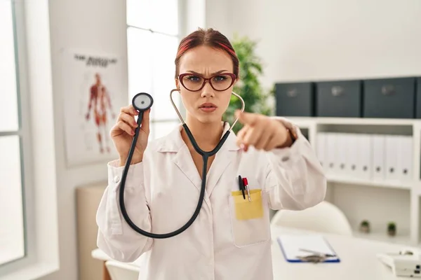 Young Caucasian Woman Wearing Doctor Uniform Using Stethoscope Pointing Finger — Stock fotografie