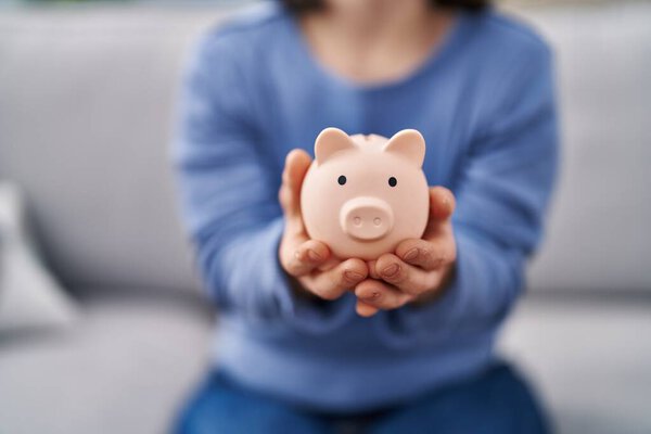 Young woman with down syndrome holding piggy bank sitting on sofa at home