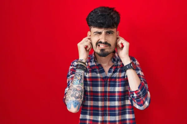 Young Hispanic Man Beard Standing Red Background Covering Ears Fingers — Foto Stock