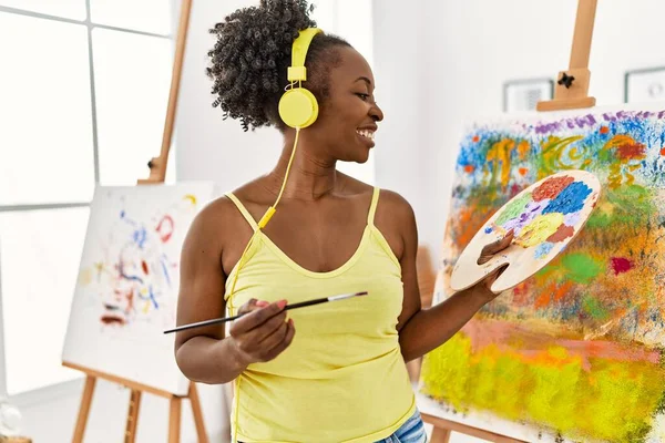 Young african american artist woman using headphones drawing at art studio.