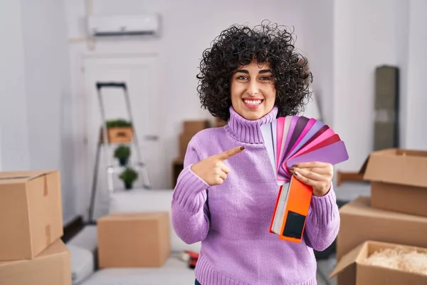 Young brunette woman with curly hair choosing color of new house wall smiling happy pointing with hand and finger 