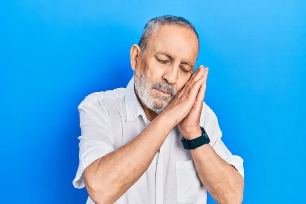 Handsome senior man with beard wearing casual white shirt sleeping tired dreaming and posing with hands together while smiling with closed eyes.