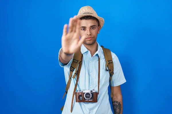 Brazilian young man holding vintage camera doing stop sing with palm of the hand. warning expression with negative and serious gesture on the face.