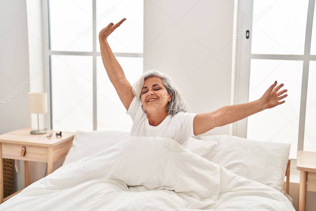 Middle age woman waking up stretching arms at bedroom