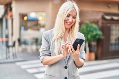 Sokakta akıllı telefon kullanan, kendine güvenen genç sarışın kadın.