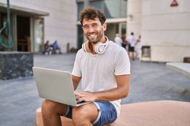 Sokakta dizüstü bilgisayar kullanarak gülümseyen İspanyol genç adam.