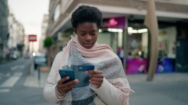 Genç Afrikalı Amerikalı kadın akıllı telefon ve kredi kartı kullanıyor.