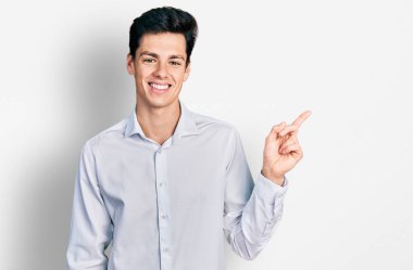 Young hispanic business man wearing business clothes with a big smile on face, pointing with hand and finger to the side looking at the camera. 