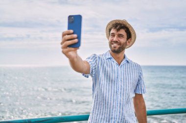 Genç İspanyol gülümseyen adam sahildeki akıllı telefonun yanında selfie çekerken mutlu oluyor.