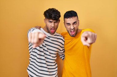 Sarı arka planda dikilen genç İspanyol eşcinsel çift kameraya kızgın ve sinirli bir şekilde bakıyor. 