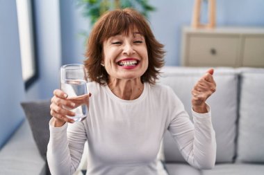 Orta yaşlı kadın bir bardak su içiyor gururla bağırıyor, zaferi kutluyor ve başarıyı kollarını kaldırarak kutluyor. 
